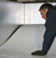 A contractor installing TerraBlock™ floor insulation in a Latham crawl space