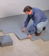 Contractors installing basement subfloor tiles and matting on a concrete basement floor in Colonie, New York